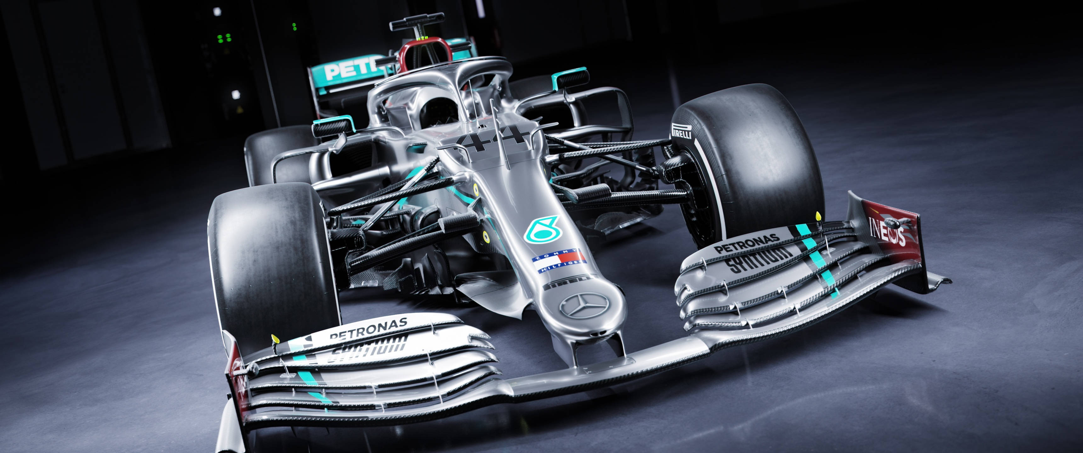 F1 桌布 壁紙 — 一架流線型銀色賓士一級方程式賽車，帶有青綠色點綴和贊助商標誌，在昏暗的攝影棚中以戲劇性燈光展示。