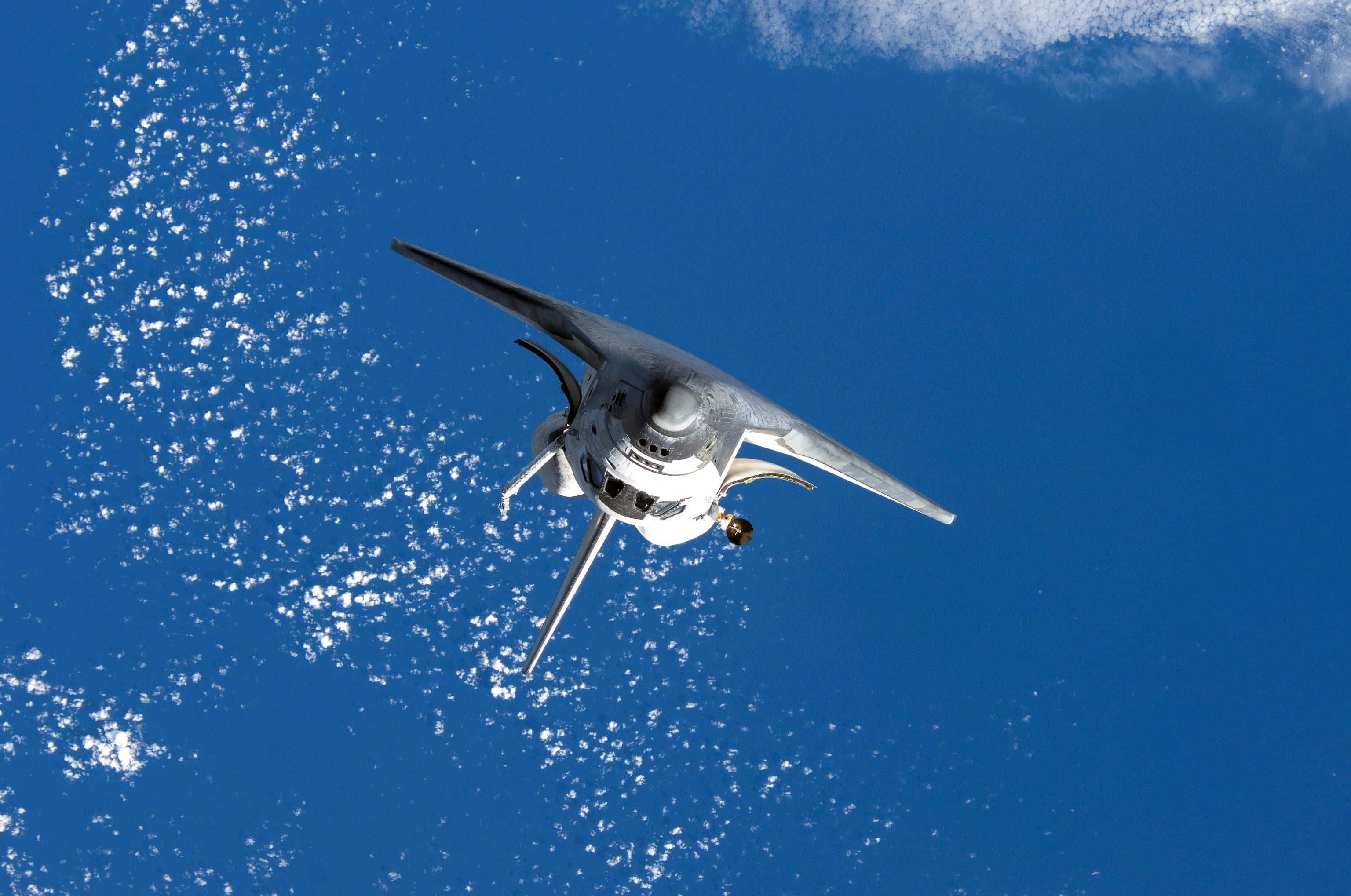 space shuttle 桌布 壁紙 — 一架流線型銀色飛機翱翔於點綴著散落白雲的湛藍海洋之上。