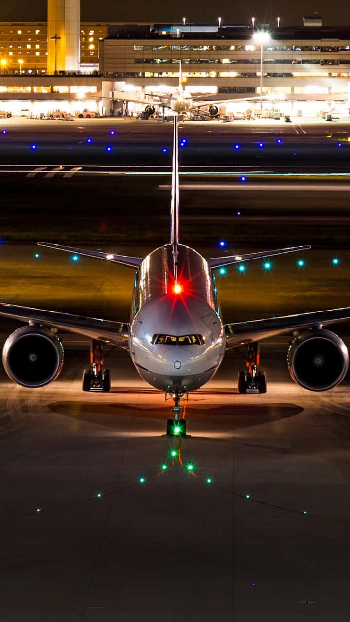 Airport 桌布 壁紙 — 一架流線型飛機在夜間停在跑道上，背景有發光的燈光和明亮的航廈。