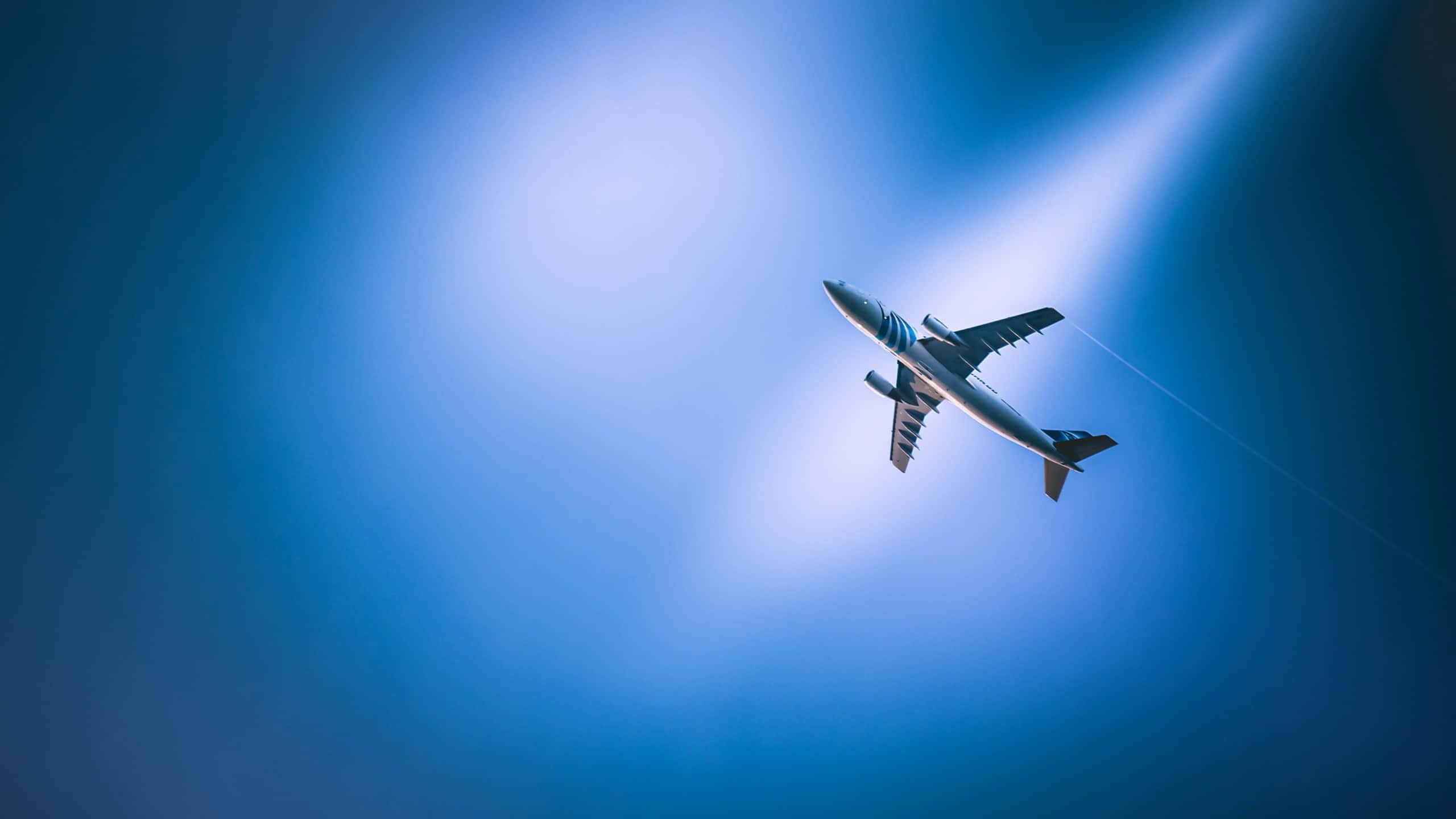 Aircraft 桌布 壁紙 — 一架流線型飛機在燦爛的藍天中向上翱翔，被明亮的陽光照射。