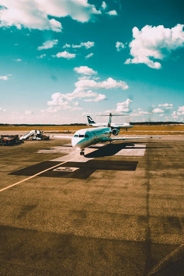 飛機 桌布 壁紙 — 一架流線型飛機在陽光普照的停機坪上，背景是點綴著蓬鬆白雲的湛藍天空。