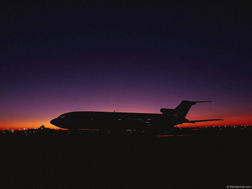 飛機 桌布 壁紙 — 一架流線型飛機的剪影停在跑道上，暮色將天空染成深紫色和火橙色。