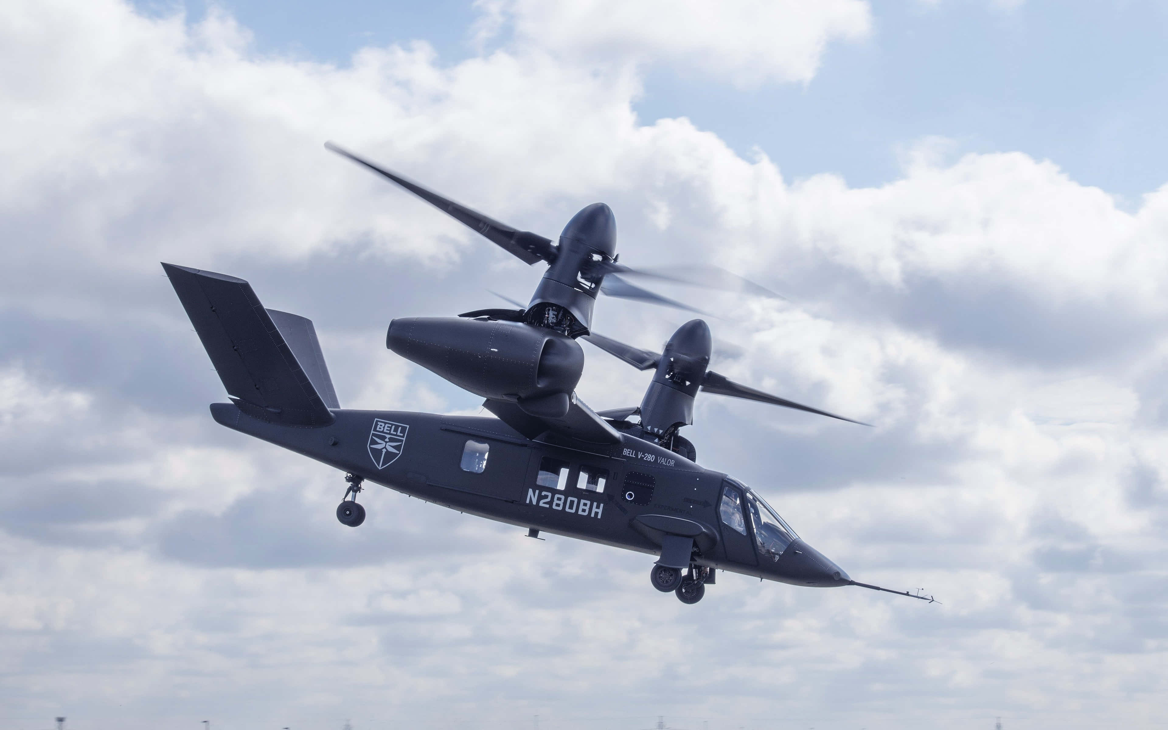 4K Helicopters 桌布 壁紙 — 一架流線型黑色Bell V-280 Valor傾轉旋翼機在部分多雲的天空翱翔，起落架已放下。