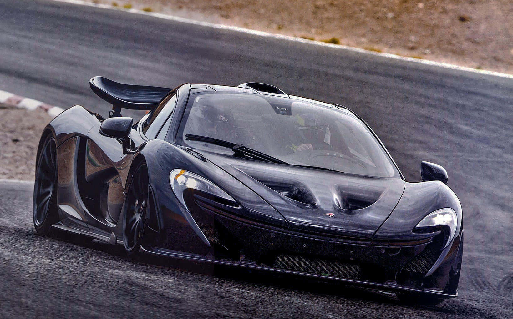 麥拉倫 桌布 壁紙 — 一架流線型黑色McLaren P1超級跑車在賽道上飛馳，背景是模糊的瀝青路面。