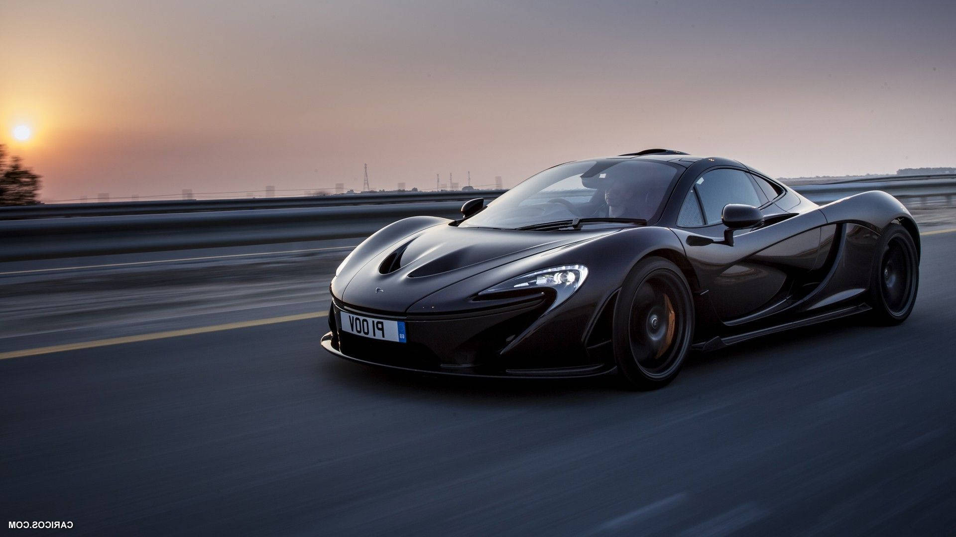 麥拉倫 桌布 壁紙 — 一架流線型黑色McLaren P1在日落時分沿高速公路飛馳，帶有動態模糊和溫暖的金色光線。