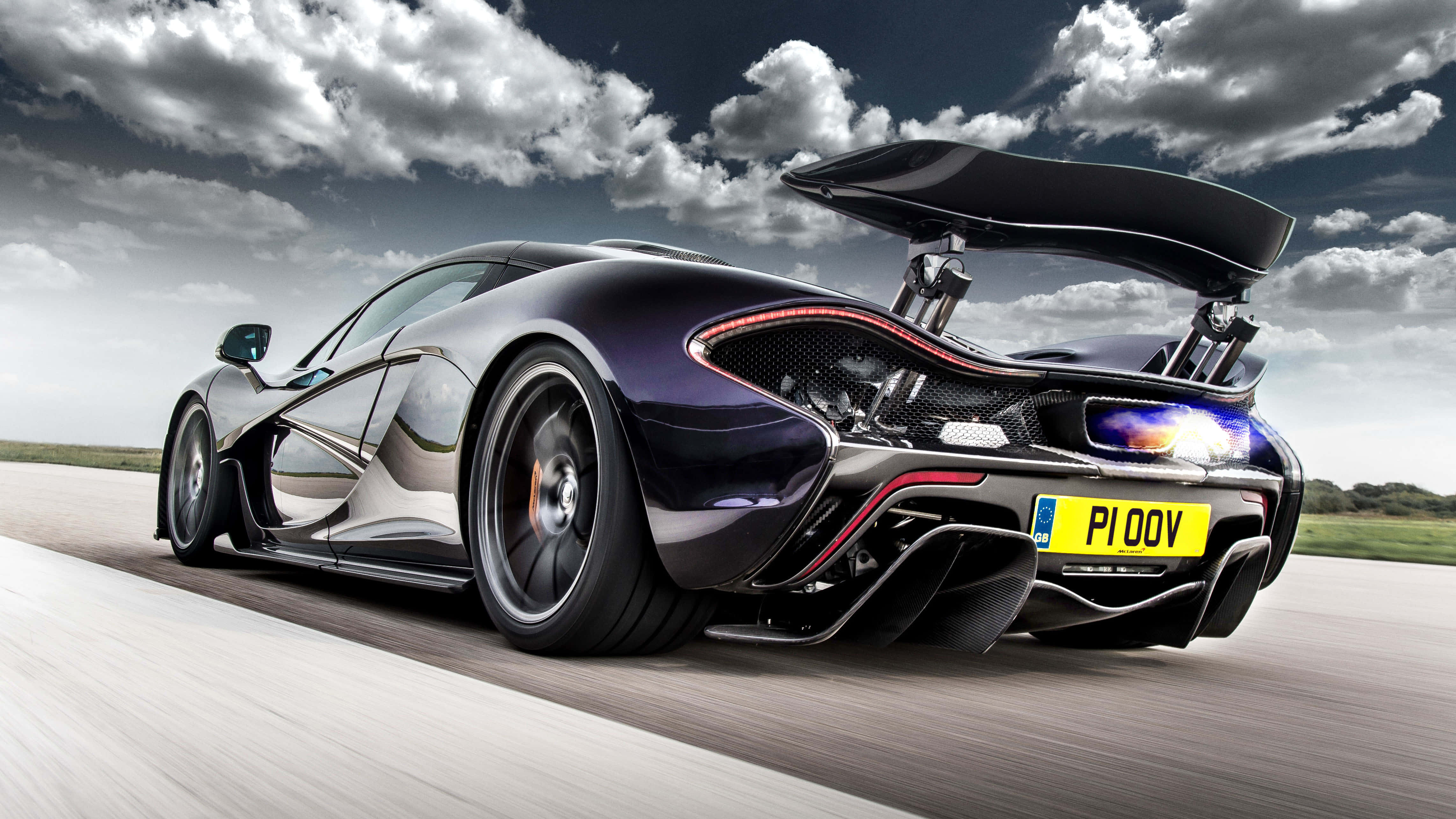 麥拉倫 桌布 壁紙 — 一架流線型黑色McLaren P1超級跑車在戲劇性的多雲天空下，尾翼升起，在跑道上疾馳。