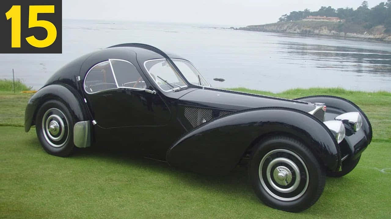Vintage Car 桌布 壁紙 — 一架流線型黑色復古Bugatti跑車在陰天下，在平靜的海洋旁的草地上閃閃發光。