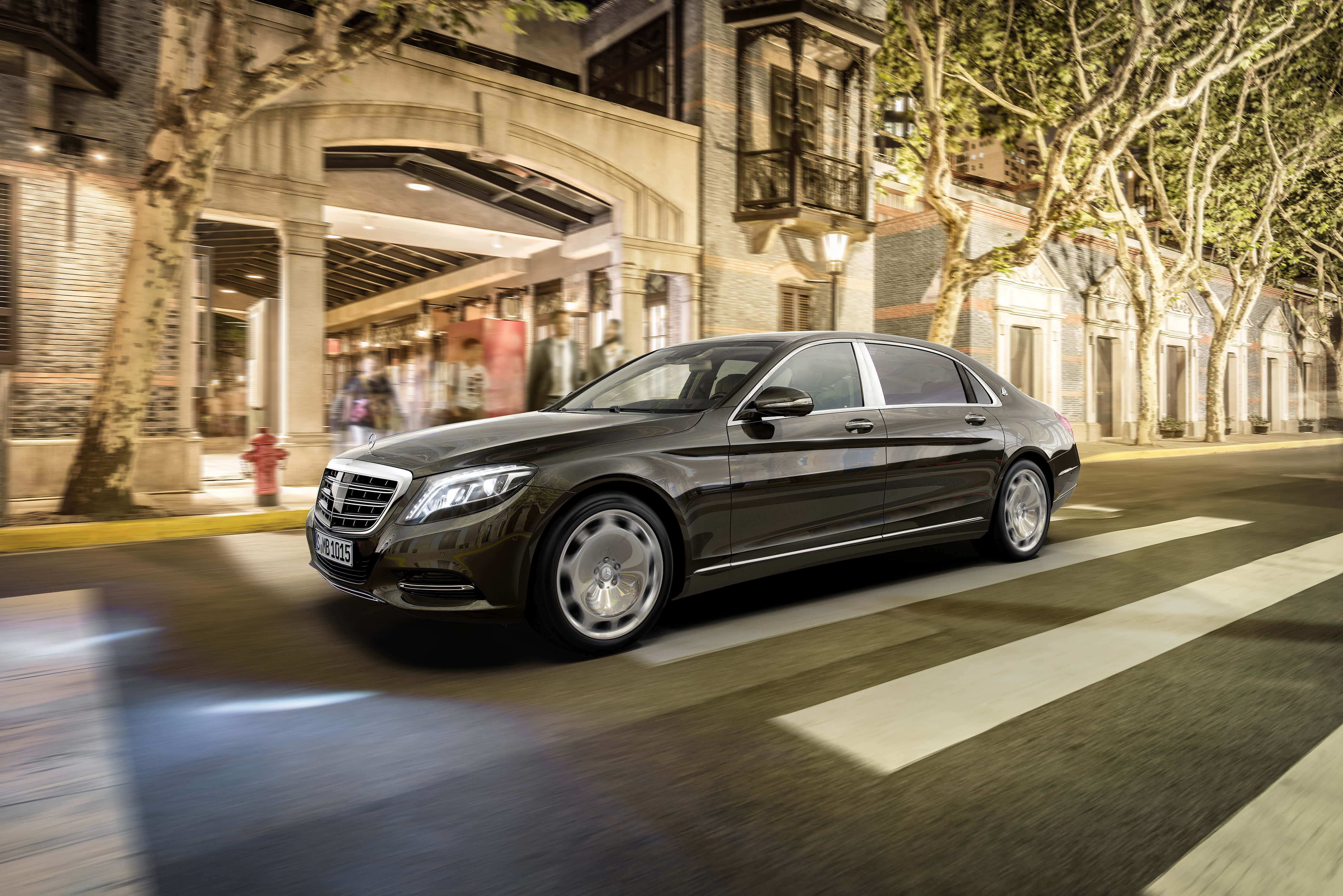 Maybach 桌布 壁紙 — 一架流線型黑色賓士S-Class轎車在夜間穿過溫暖燈光的歐洲城市街道，帶有模糊動感和發光的商店櫥窗。