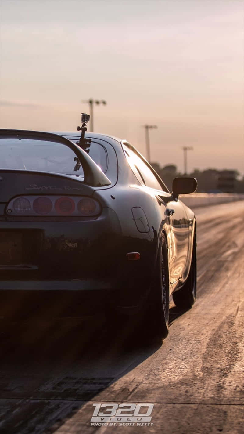 黑色跑車在直線加速賽道上於夕陽下飛馳。 — Toyota Supra Mk4 壁紙