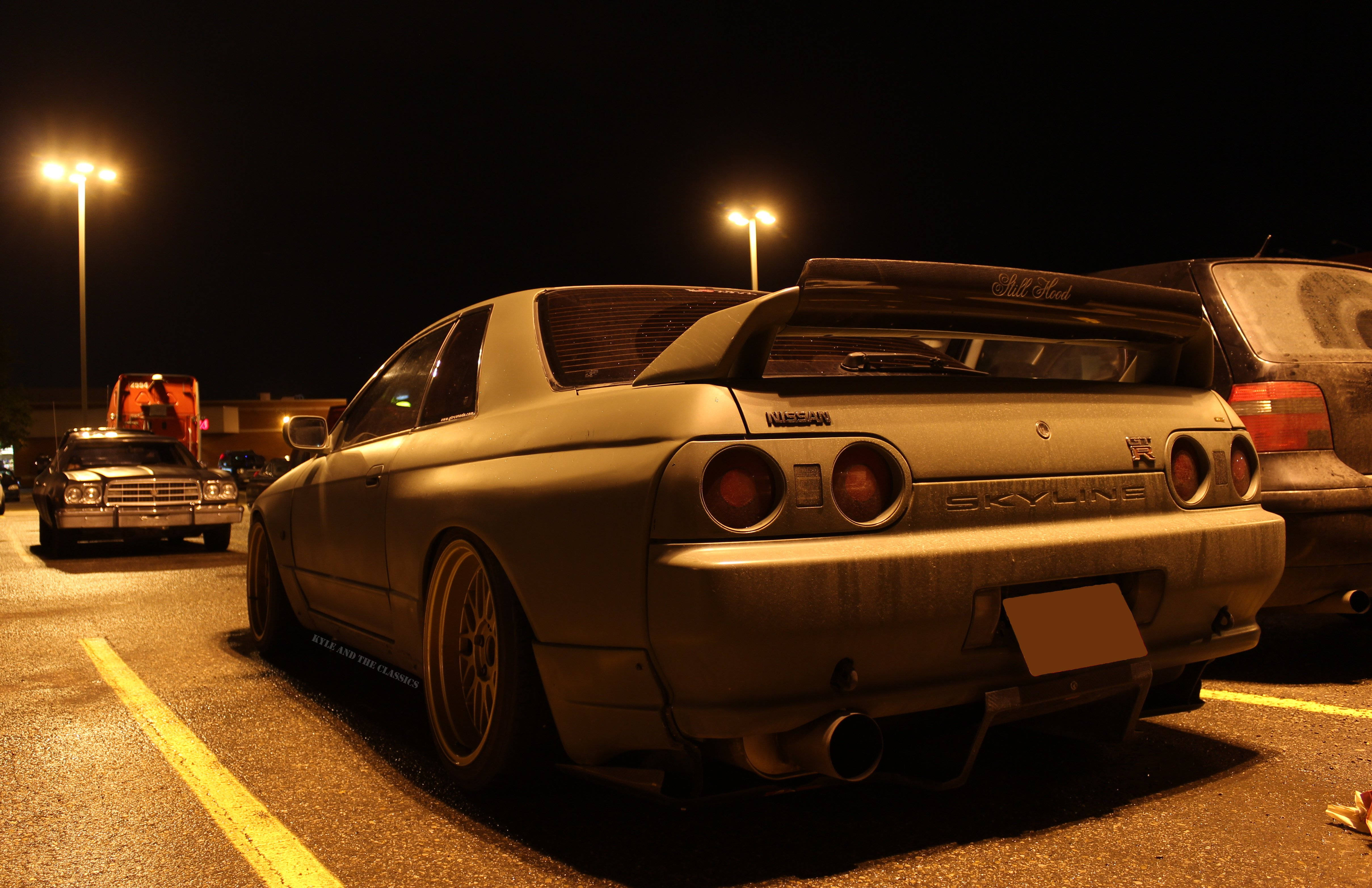 夜晚 桌布 壁紙 — 一架消光灰色日產Skyline R32在夜晚停放在燈光明亮的停車場，發光的街燈投下溫暖的陰影。