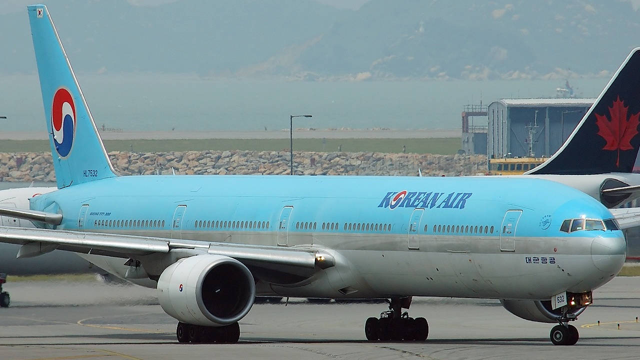  壁紙 — 一架淺藍色的大韓航空波音777停在機場停機坪上，背景有朦朧的山脈。