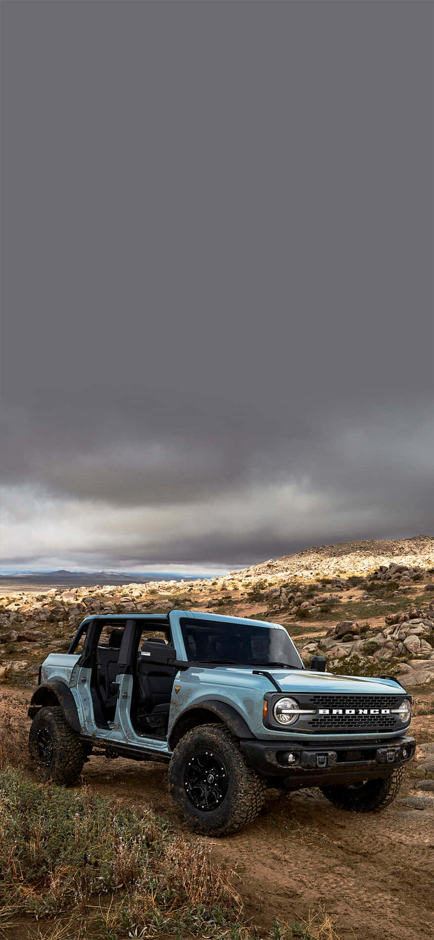 Ford Bronco 桌布 壁紙 — 一架淺藍色福特Bronco在陰沉灰暗的天空下，堅固地停在岩石沙漠小徑上。