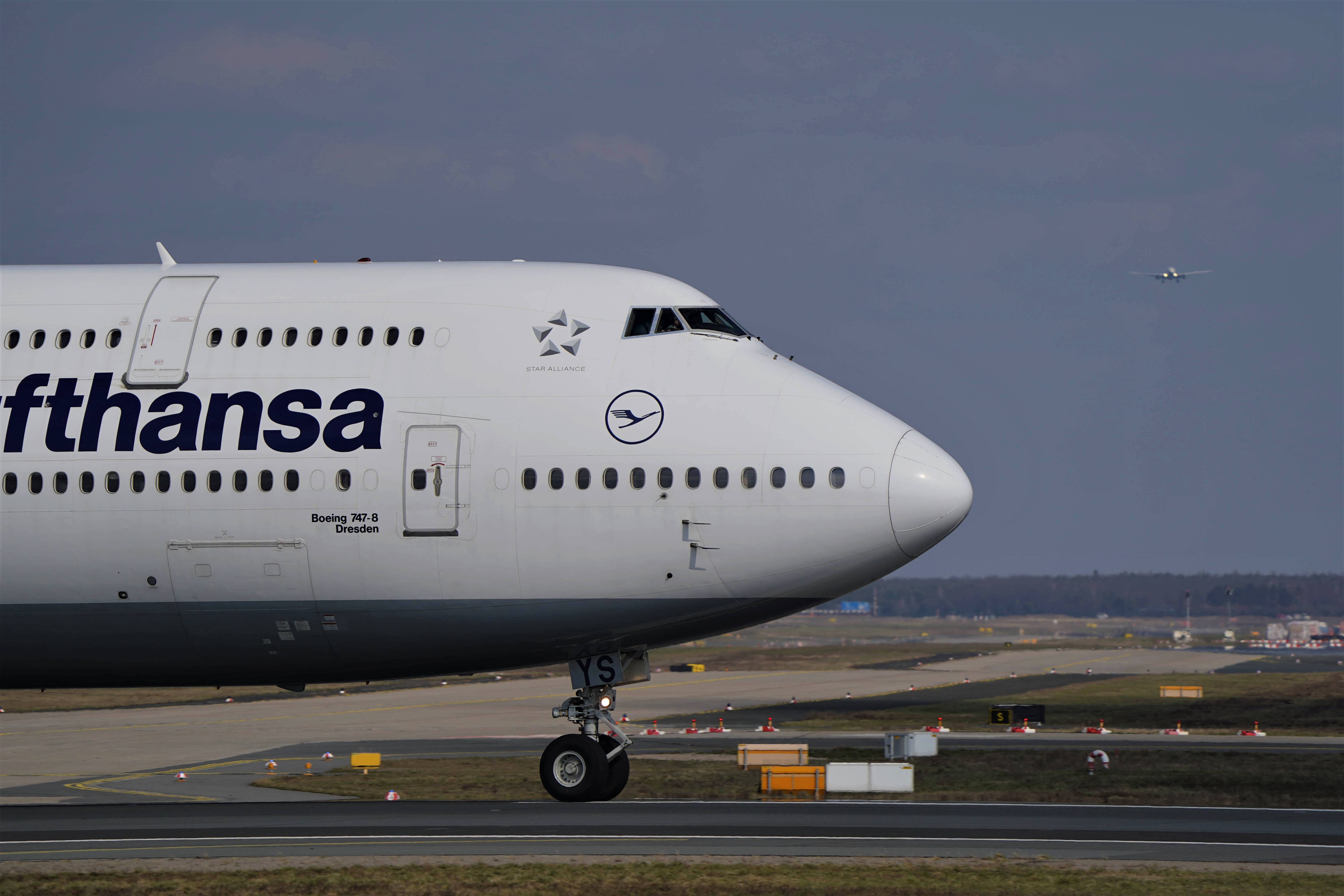 4K 飛機壁紙 桌布 壁紙 — 一架漢莎航空波音747-8停在機場停機坪上，遠處可見另一架飛機，天空多雲。