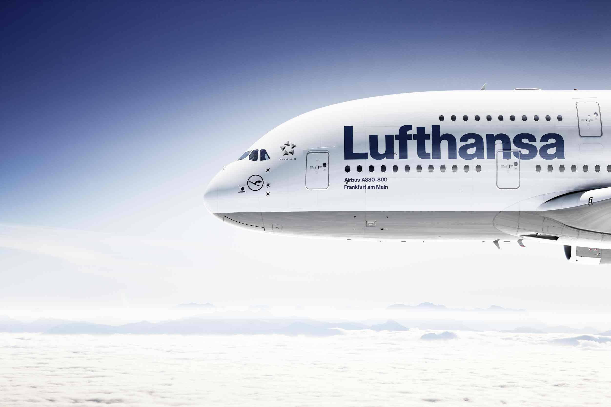 飛機 桌布 壁紙 — 一架漢莎航空空中巴士A380-800在晴朗藍天下翱翔於蓬鬆白雲之上，下方有遠山。