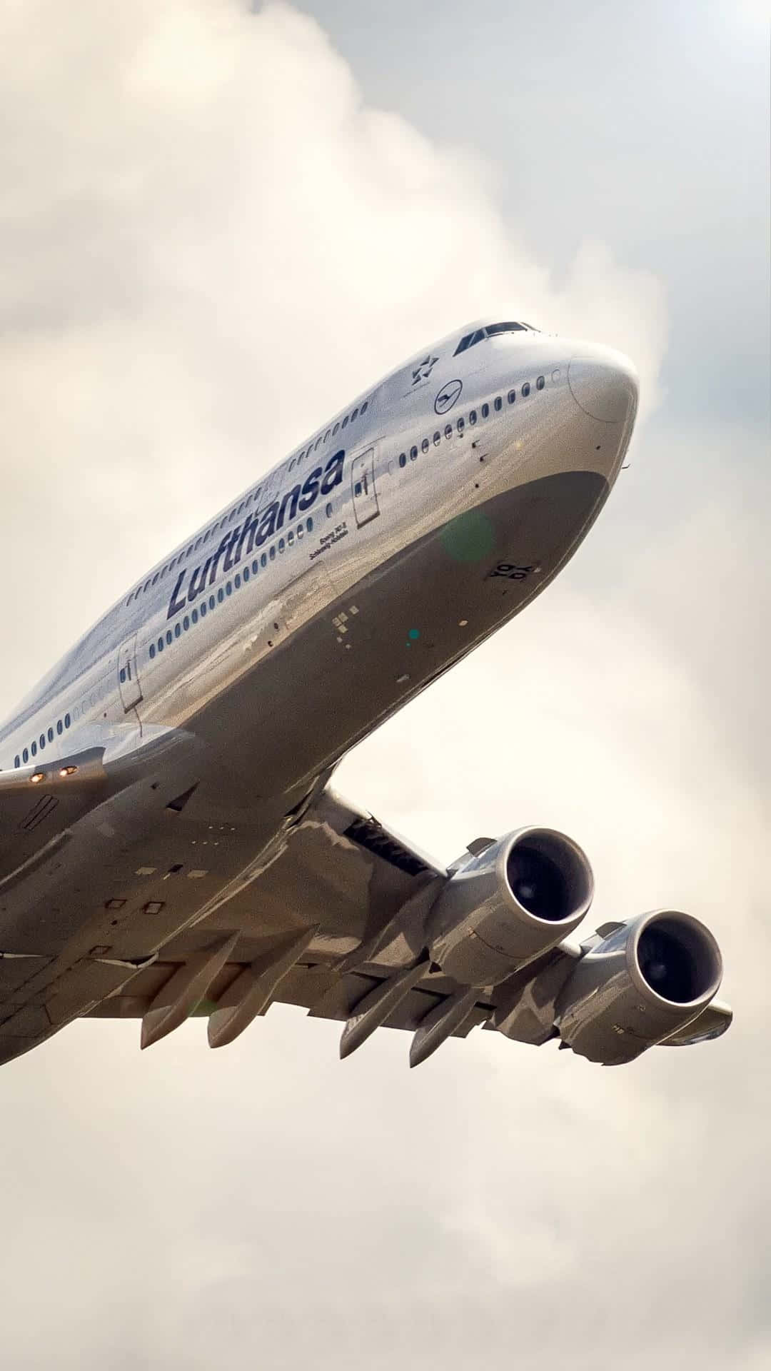 飛機 桌布 壁紙 — 一架漢莎航空空中巴士A380在陰天中翱翔，從低角度可見其巨大的引擎和四個噴射引擎。