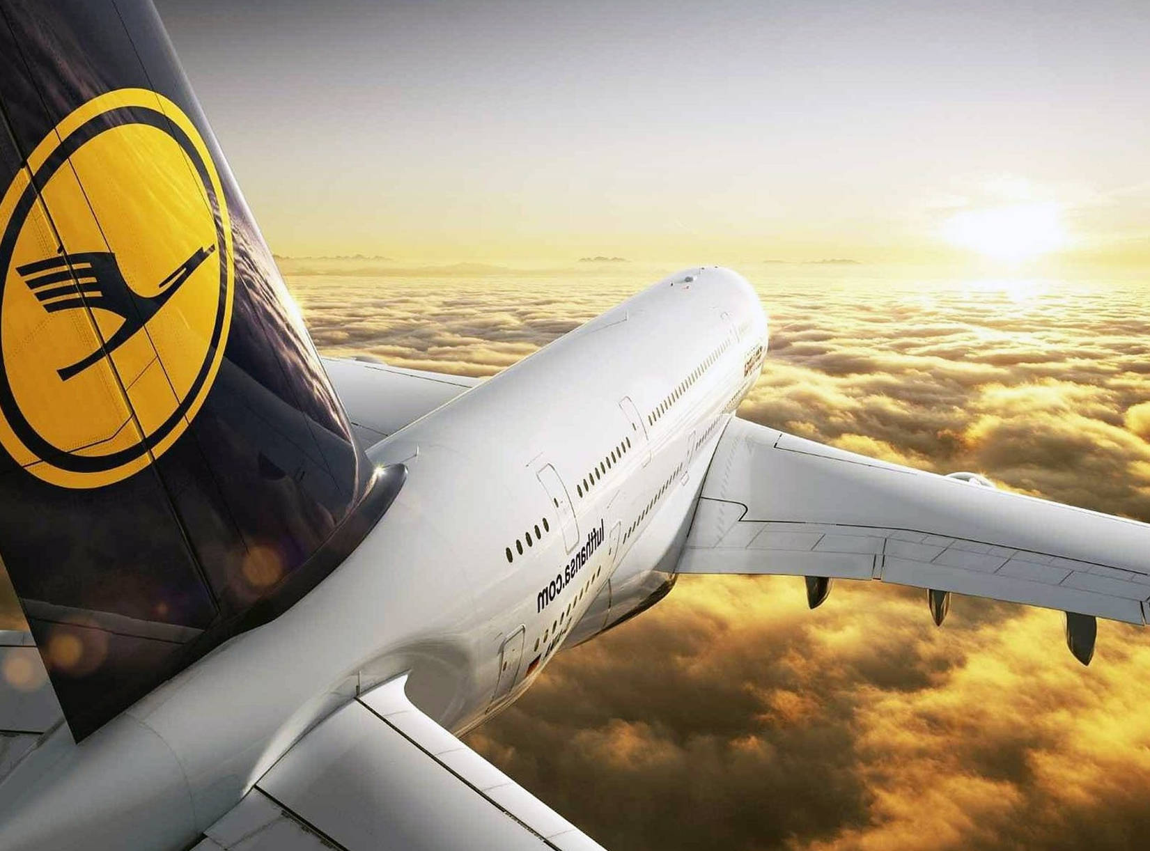 雲朵 桌布 壁紙 — 一架漢莎航空飛機在日出時翱翔於金色雲層之上，太陽在地平線上閃耀。
