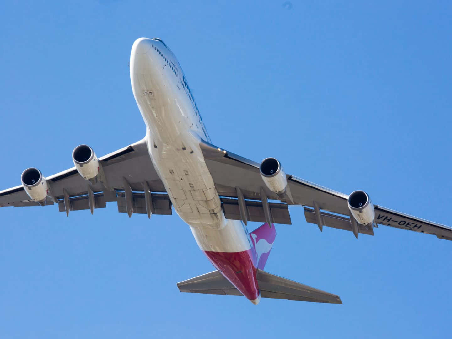  壁紙 — 一架澳洲航空波音747在晴朗藍天中翱翔，四個引擎和標誌性紅色機尾清晰可見。