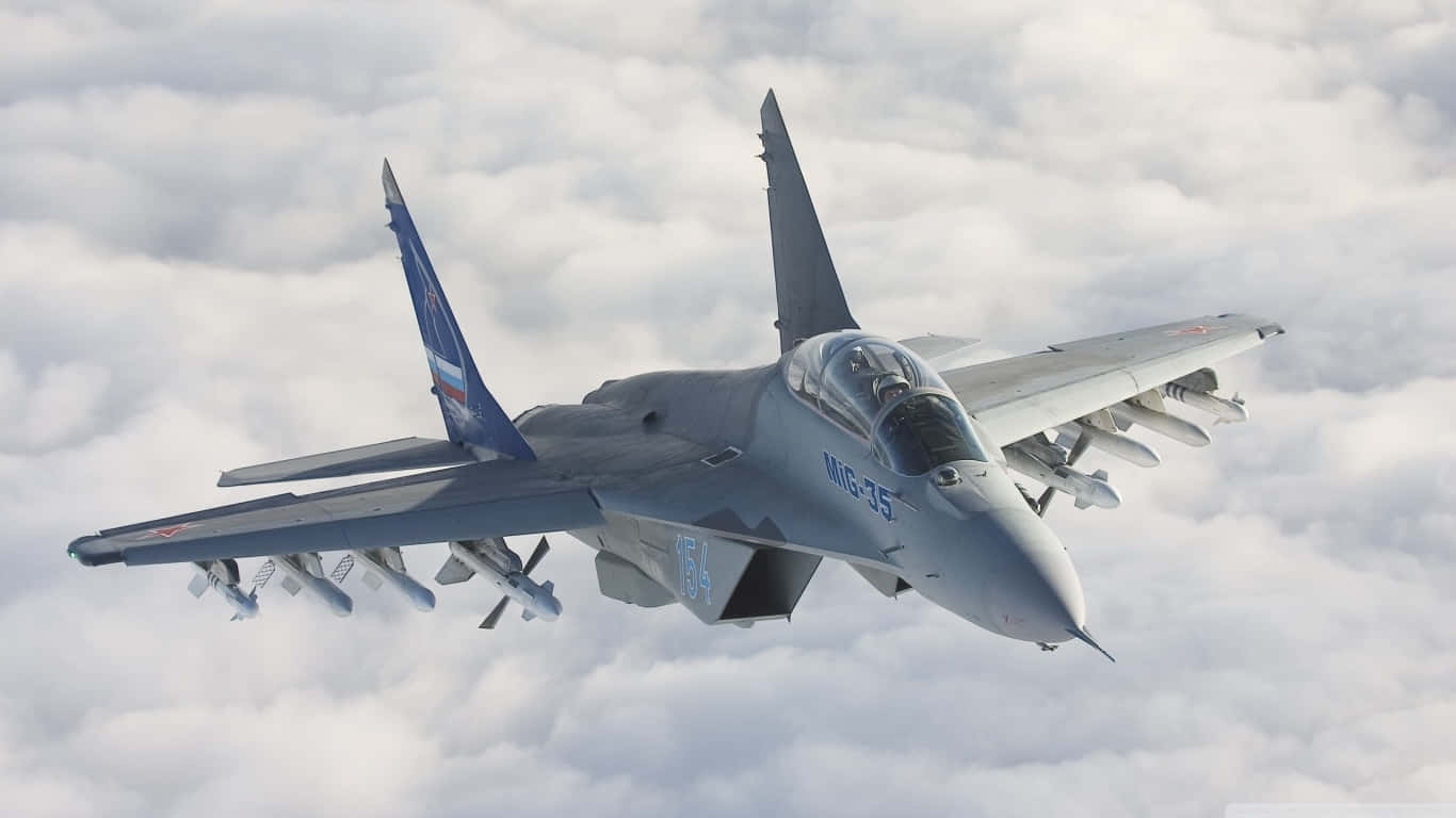 Cloudy Sky 桌布 壁紙 — 一架灰色 MiG-35 戰鬥機在蓬鬆的白雲上方翱翔，武器和駕駛艙清晰可見。