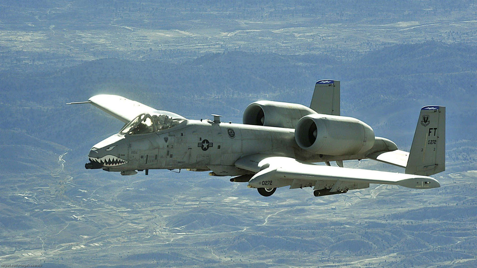A 10 Warthog 桌布 壁紙 — 一架灰色A-10雷霆二式戰鬥機在晴朗藍天下低空飛越廣闊山區地形。