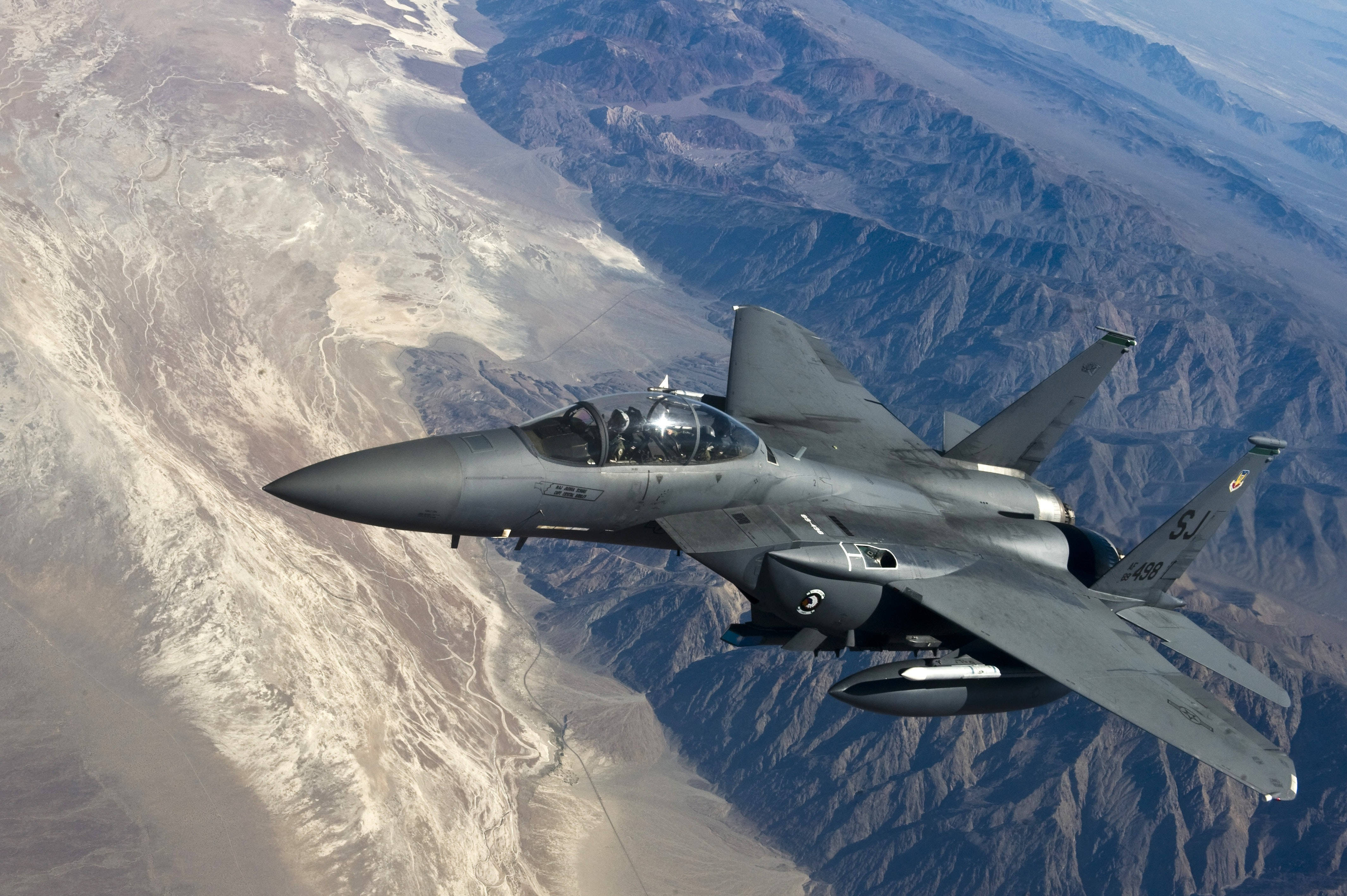 Air Force 桌布 壁紙 — 一架灰色戰鬥機在崎嶇的沙漠山脈上空翱翔，下方投下清晰的陰影。