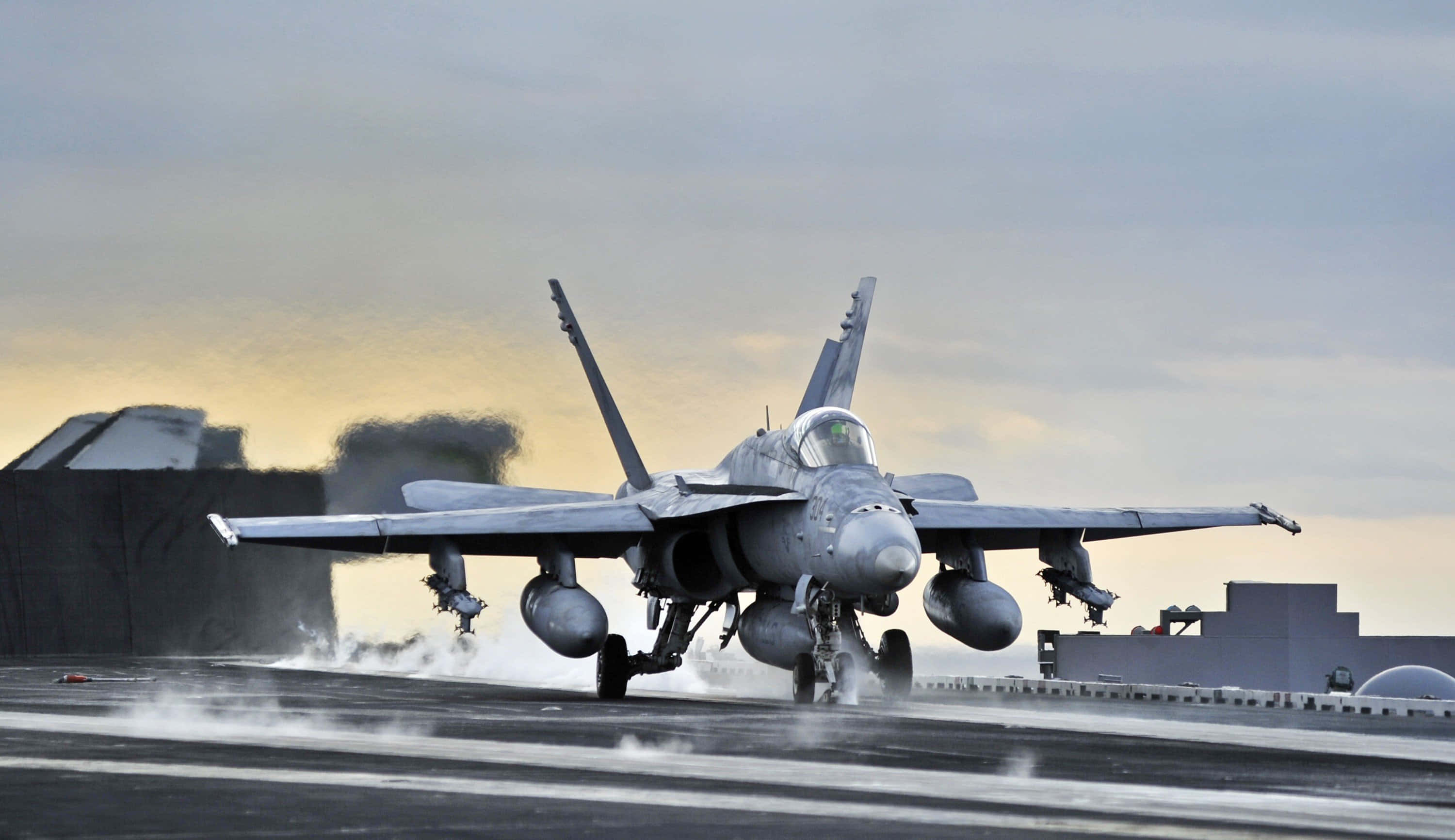 Military Plane 桌布 壁紙 — 一架灰色戰鬥機在日落時分於航空母艦甲板上加速，身後留下煙霧。