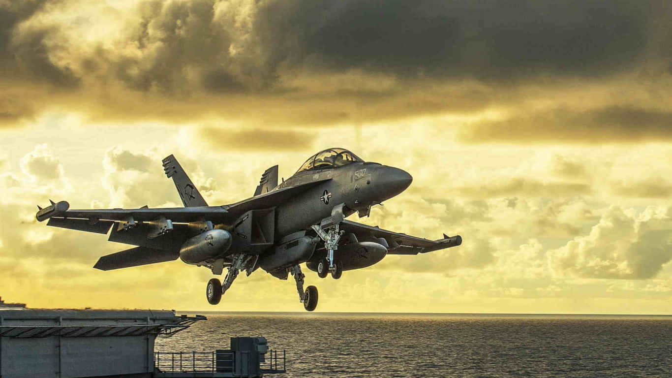 Navy 桌布 壁紙 — 一架灰色戰鬥機在日落時從航空母艦上起飛，下方是金色雲彩和海洋。