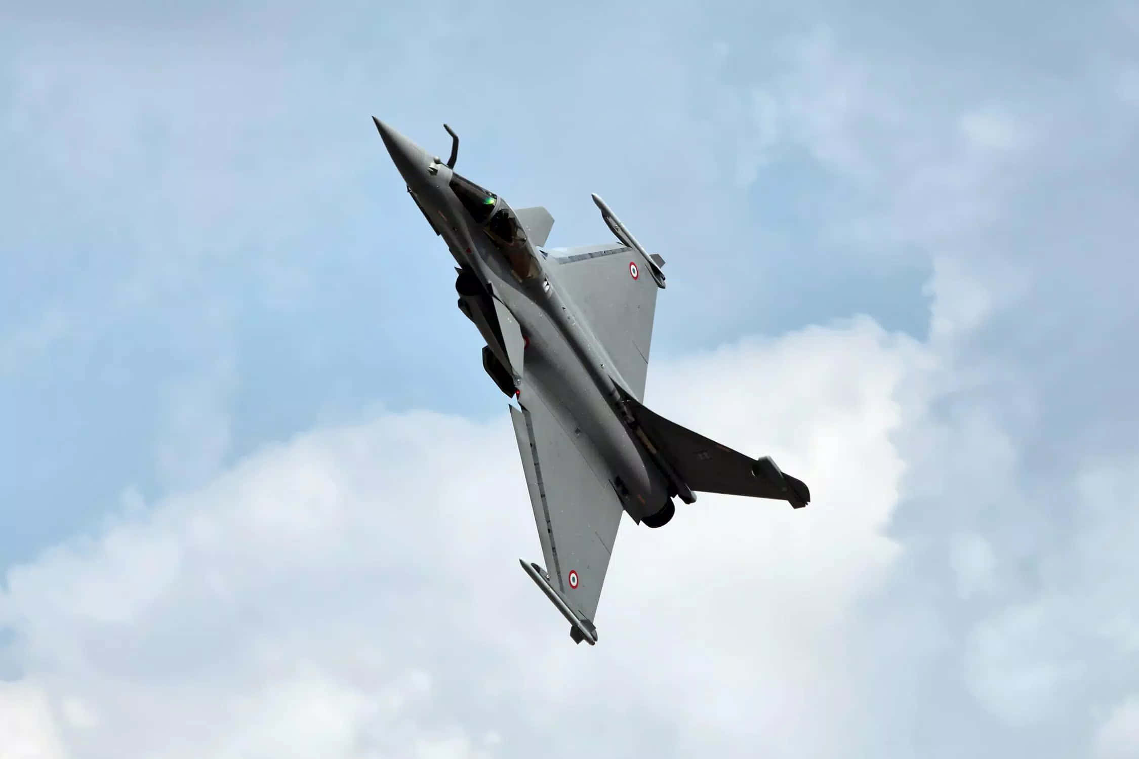Fighter Jet 桌布 壁紙 — 一架灰色戰鬥機在柔和藍天和蓬鬆白雲的背景下向上翱翔。