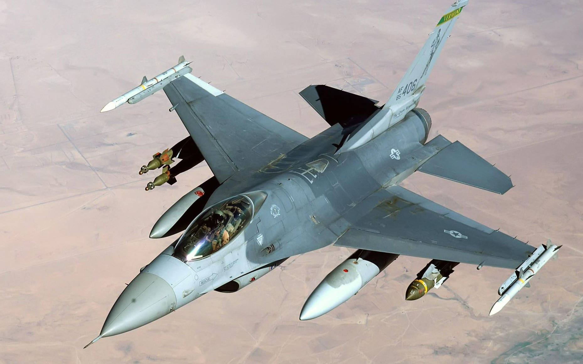 Iraq 桌布 壁紙 — 一架灰色戰鬥機在沙漠景觀上空翱翔，機翼下攜帶飛彈和炸彈。