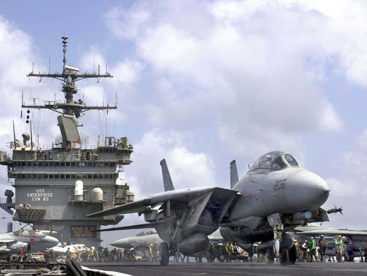 Navy 桌布 壁紙 — 一架灰色戰鬥機在部分多雲的天空下，停泊在USS企業號航空母艦的甲板上。
