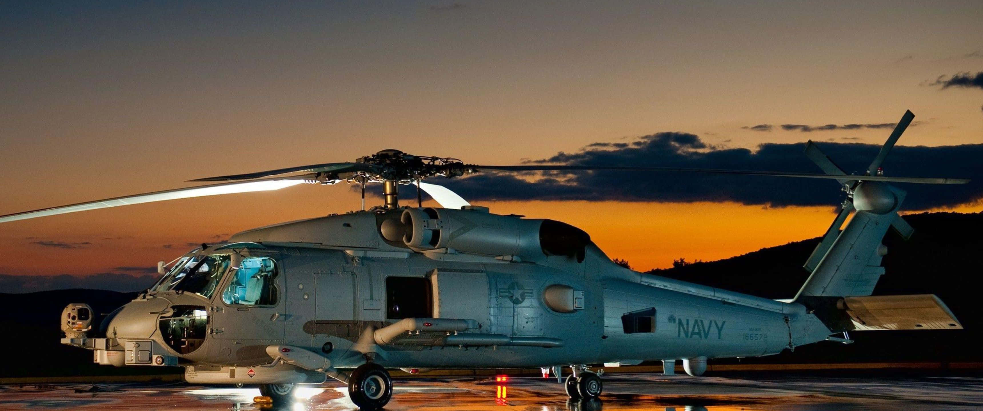 3440x1440p Helicopters 桌布 壁紙 — 一架灰色海軍直升機停在濕滑的停機坪上，金色夕陽的光芒灑滿背後的天空。