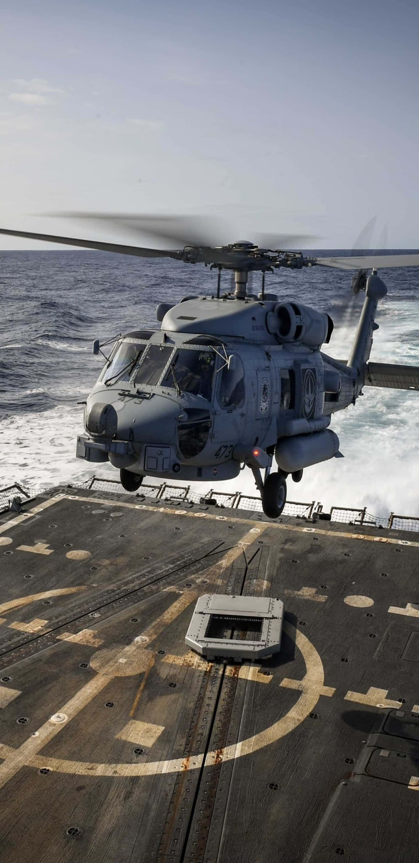 Helicopter 桌布 壁紙 — 一架灰色軍用直升機在軍艦甲板上方盤旋，下方海浪在晴朗天空下拍打。