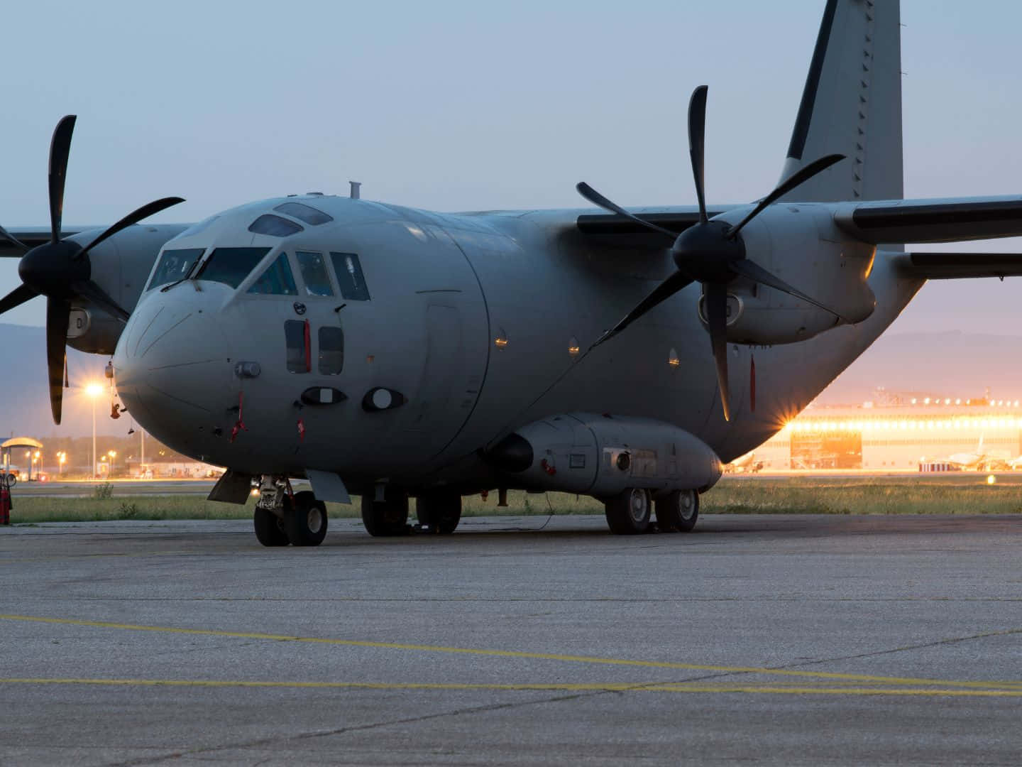 Military Plane 桌布 壁紙 — 一架灰色軍用運輸機在黃昏時分停在機場停機坪上，背景中跑道燈閃爍。