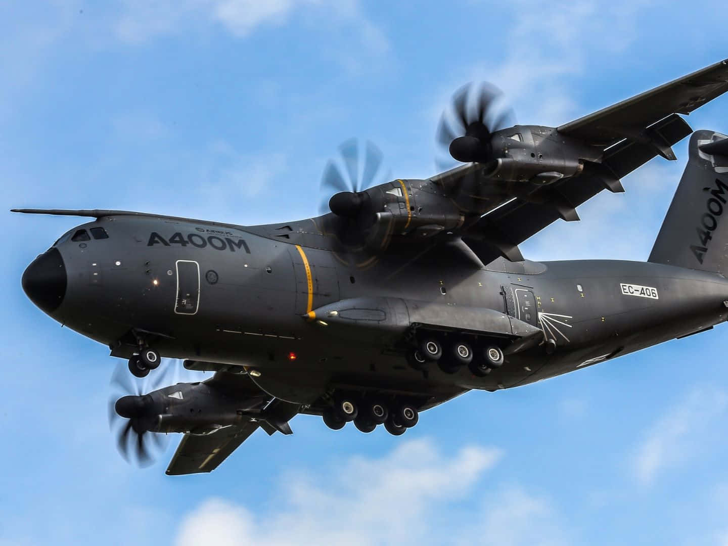 Aircraft 桌布 壁紙 — 一架灰色軍用運輸機配備四個螺旋槳，在晴朗藍天中翱翔，天空有零星雲朵。
