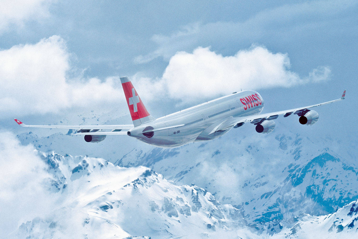 飛機 桌布 壁紙 — 一架瑞士空中巴士A380在部分多雲的藍天下，優雅地翱翔於積雪的山峰之上。