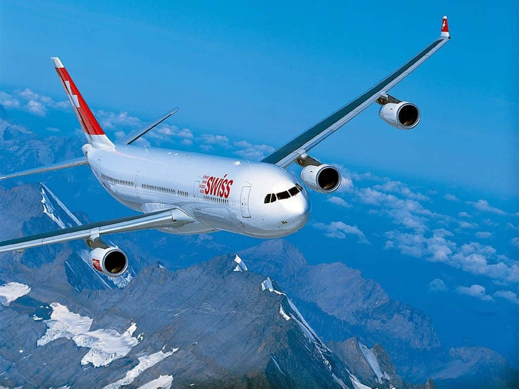 飛機 桌布 壁紙 — 一架瑞士航空的空中巴士A340在晴朗藍天與散雲下翱翔於積雪的山峰之上。