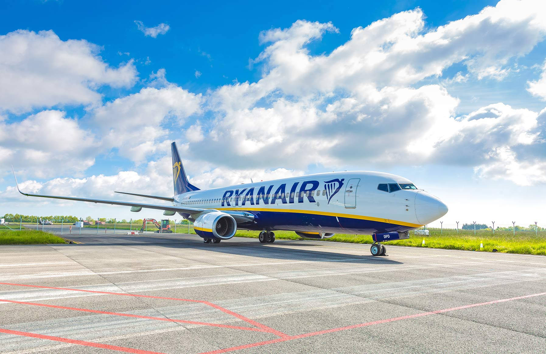 雲朵 桌布 壁紙 — 一架瑞安航空飛機停在陽光明媚的停機坪上，背景是晴朗的藍天和蓬鬆的白雲。