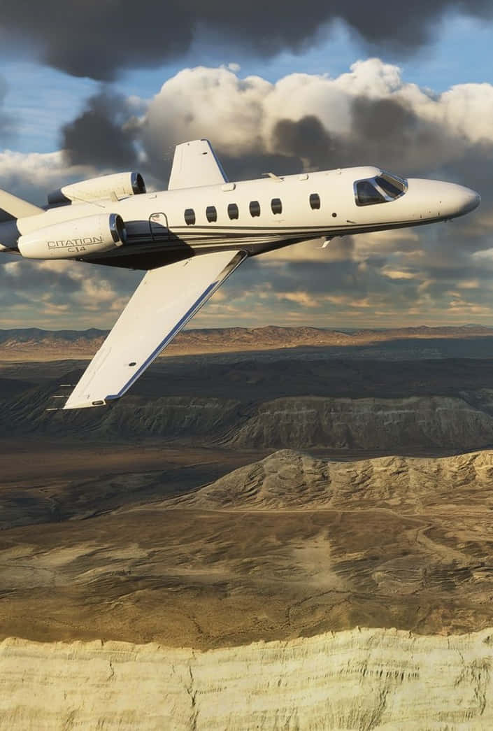 Android Microsoft Flight Simulator 桌布 壁紙 — 一架白色 Citation CJ4 私人飛機在戲劇性的多雲天空下，翱翔於崎嶇的沙漠峽谷之上。