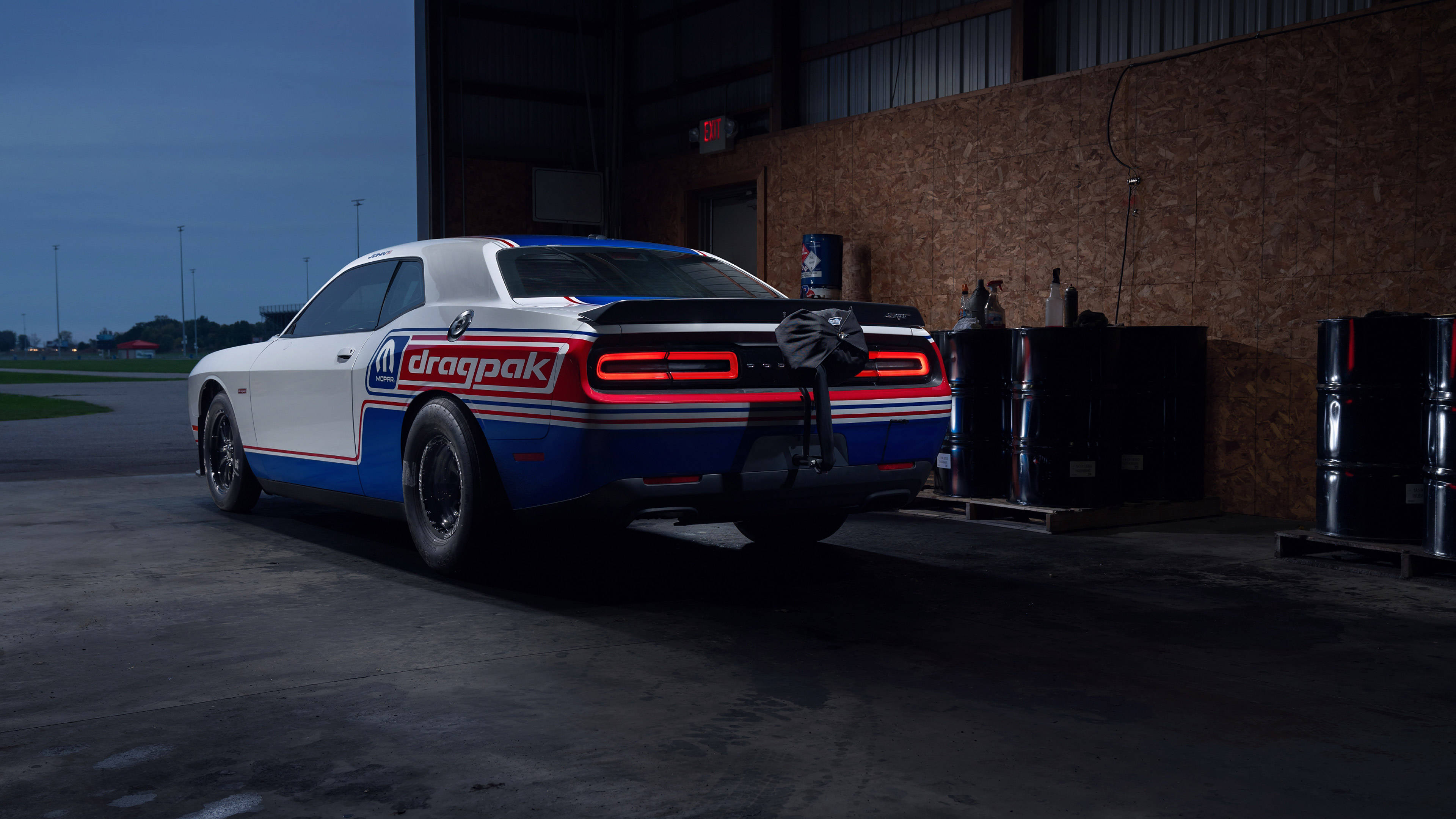 Challenger 桌布 壁紙 — 一架白色、藍色和紅色的直線加速賽車 Dodge Challenger，帶有發光的尾燈，在黃昏時停放在光線昏暗的車庫中。