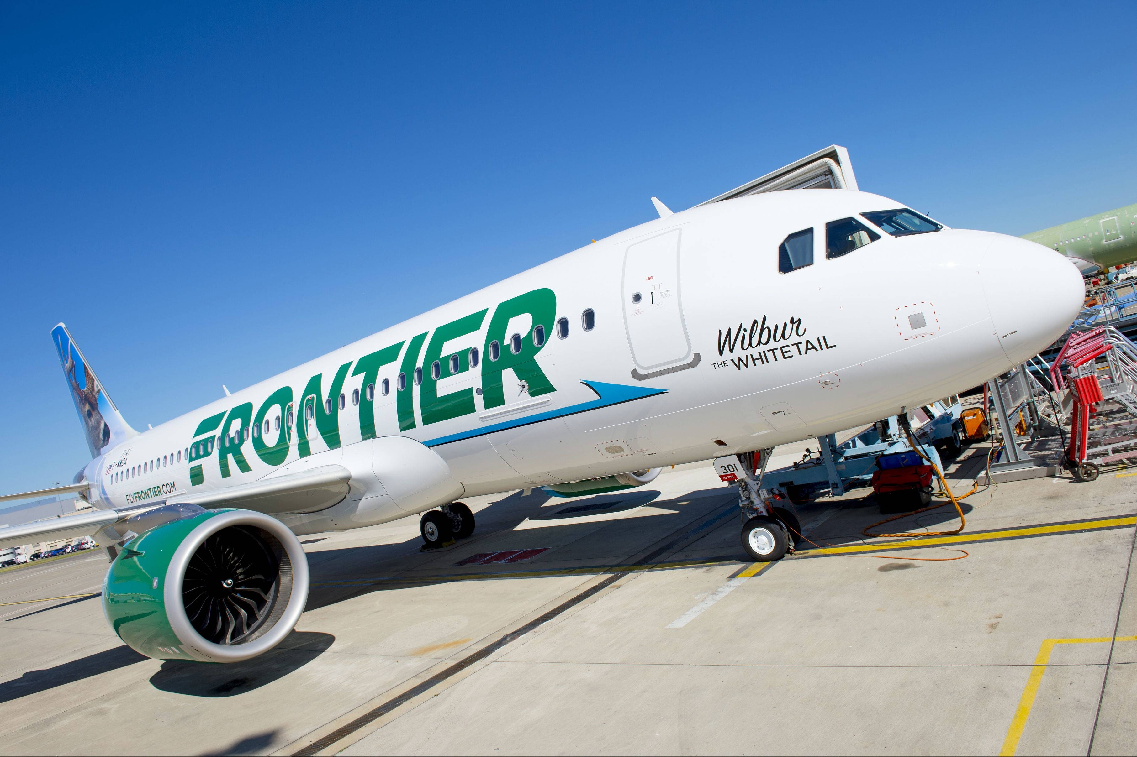 transportation 桌布 壁紙 — 一架白色Frontier Airlines飛機，帶有綠色字樣，停在陽光普照的停機坪上，天空湛藍。