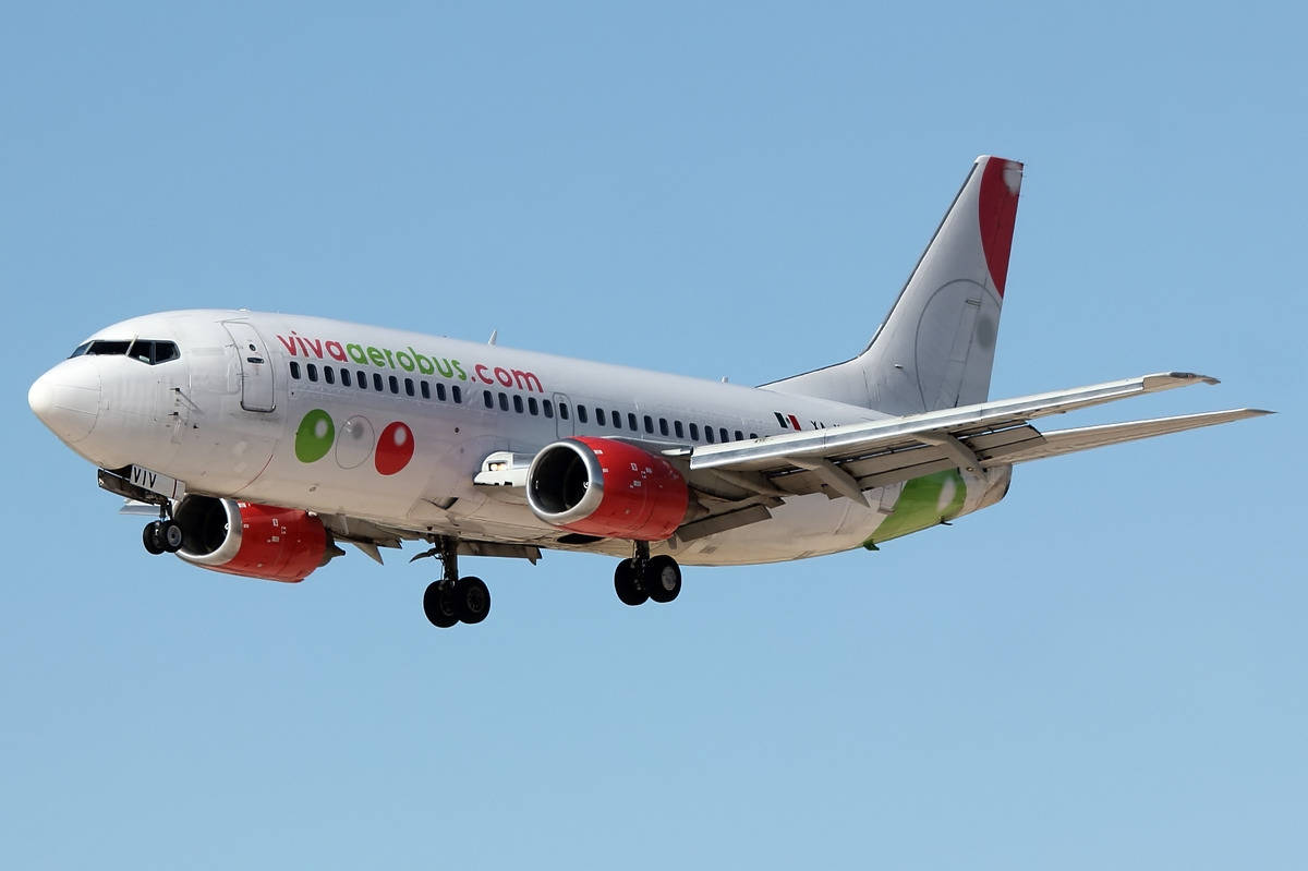 飛機 桌布 壁紙 — 一架白色Viva Aerobus飛機，配備紅色引擎和彩色標誌，在白天晴朗的藍天下飛行。