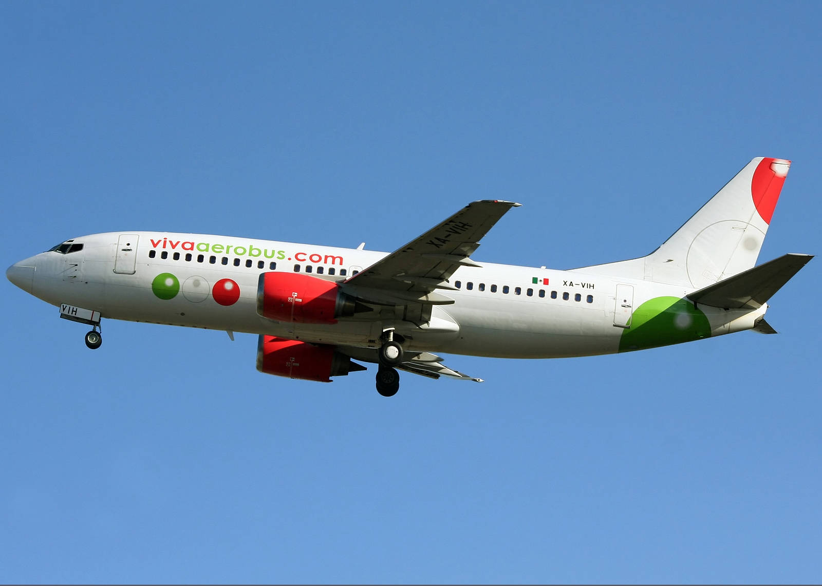 飛機 桌布 壁紙 — 一架白色Viva Aerobus飛機，帶有紅、綠、白塗裝，起落架放下，在清澈的藍天中飛行。