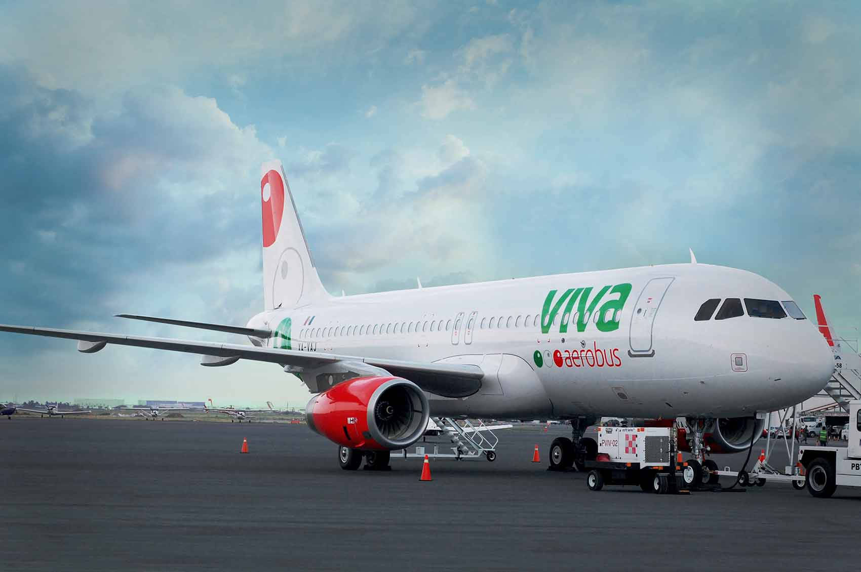 Airport 桌布 壁紙 — 一架白色Viva Aerobus飛機，紅色引擎，停在停機坪上，天空多雲，附近有地勤人員和設備。