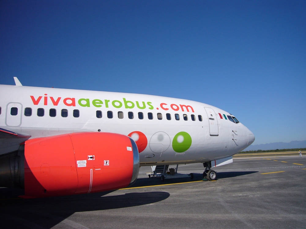 Airport 桌布 壁紙 — 一架白色Viva Aerobus飛機，帶有紅色引擎和彩色標誌，停在晴朗藍天下的陽光機場停機坪上。