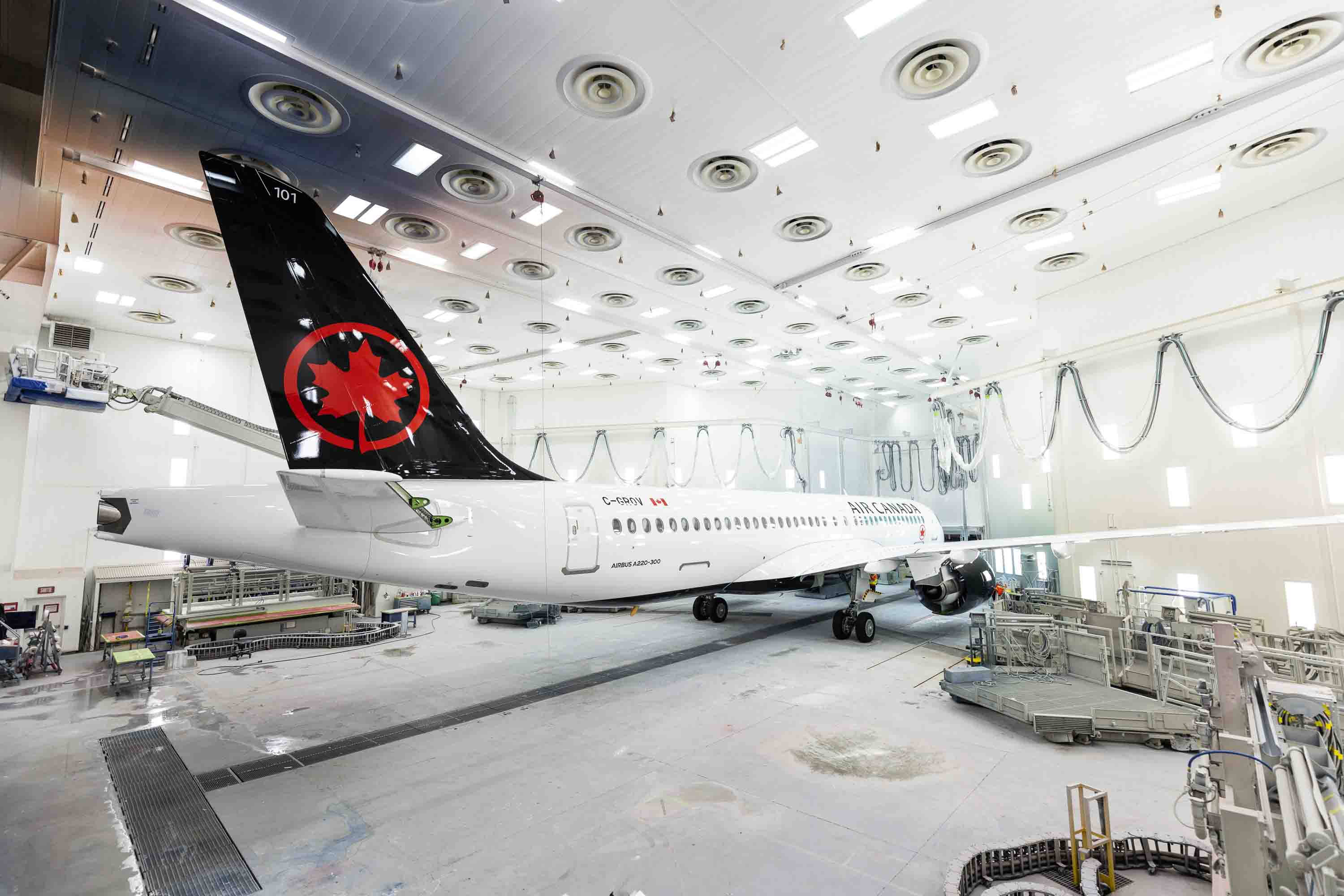 Airport 桌布 壁紙 — 一架白色加拿大航空飛機，帶有紅色楓葉尾翼，懸掛在明亮的工業機庫中進行維護。