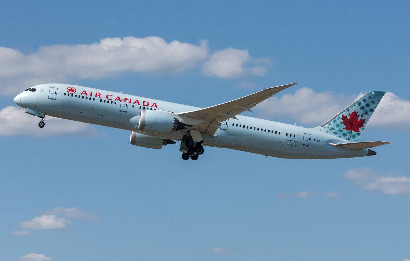  壁紙 — 一架白色和紅色塗裝的加拿大航空波音787夢想客機在晴朗的藍天中翱翔，伴隨著蓬鬆的白雲。