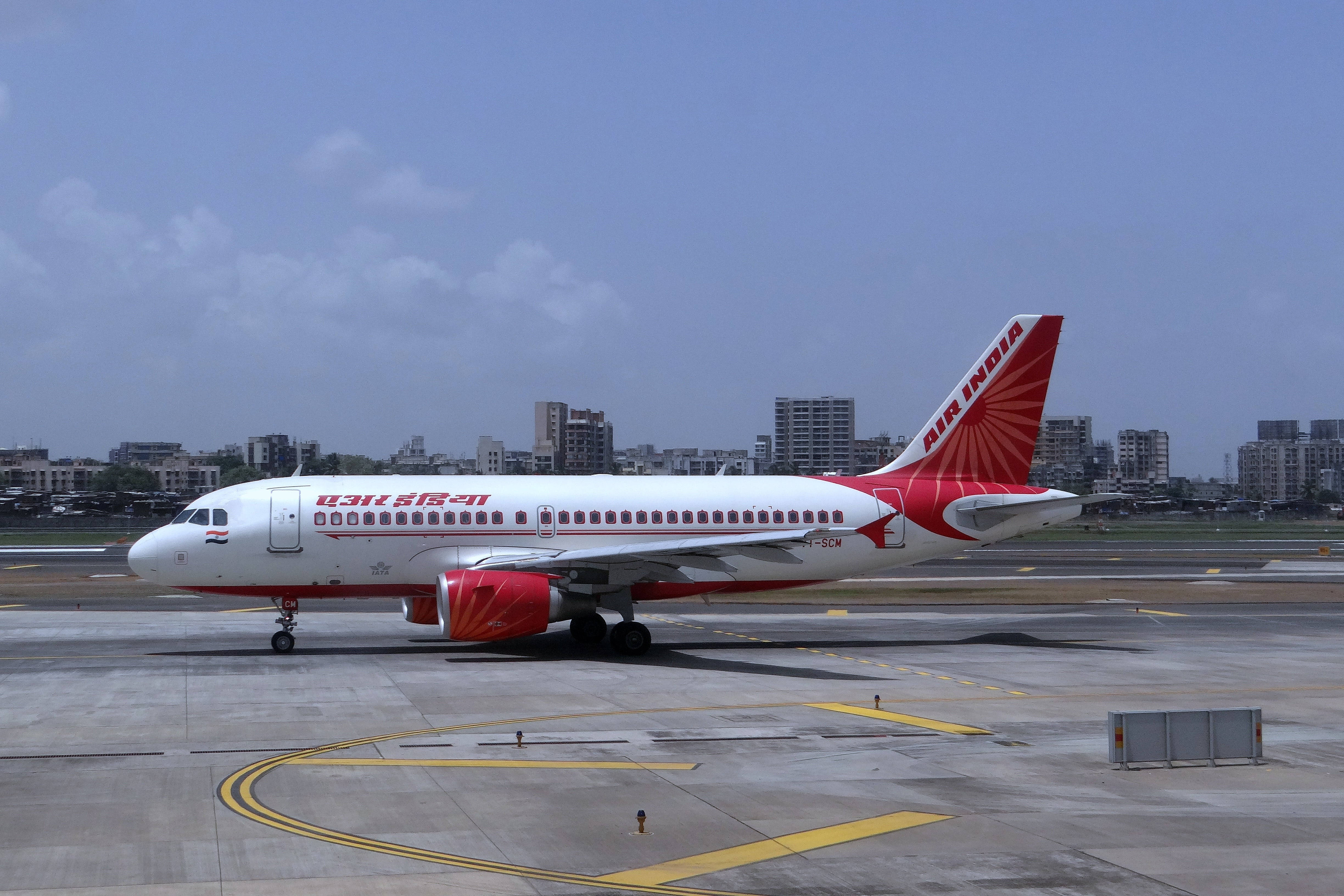 Mumbai 桌布 壁紙 — 一架白色和紅色塗裝的印度航空客機停在停機坪上，背景是城市建築，天空部分多雲。
