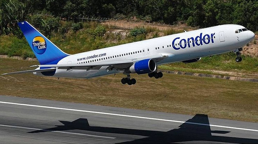 Airport 桌布 壁紙 — 一架白色和藍色塗裝的Condor Thomas Cook飛機在綠色山丘背景下降落在跑道上。