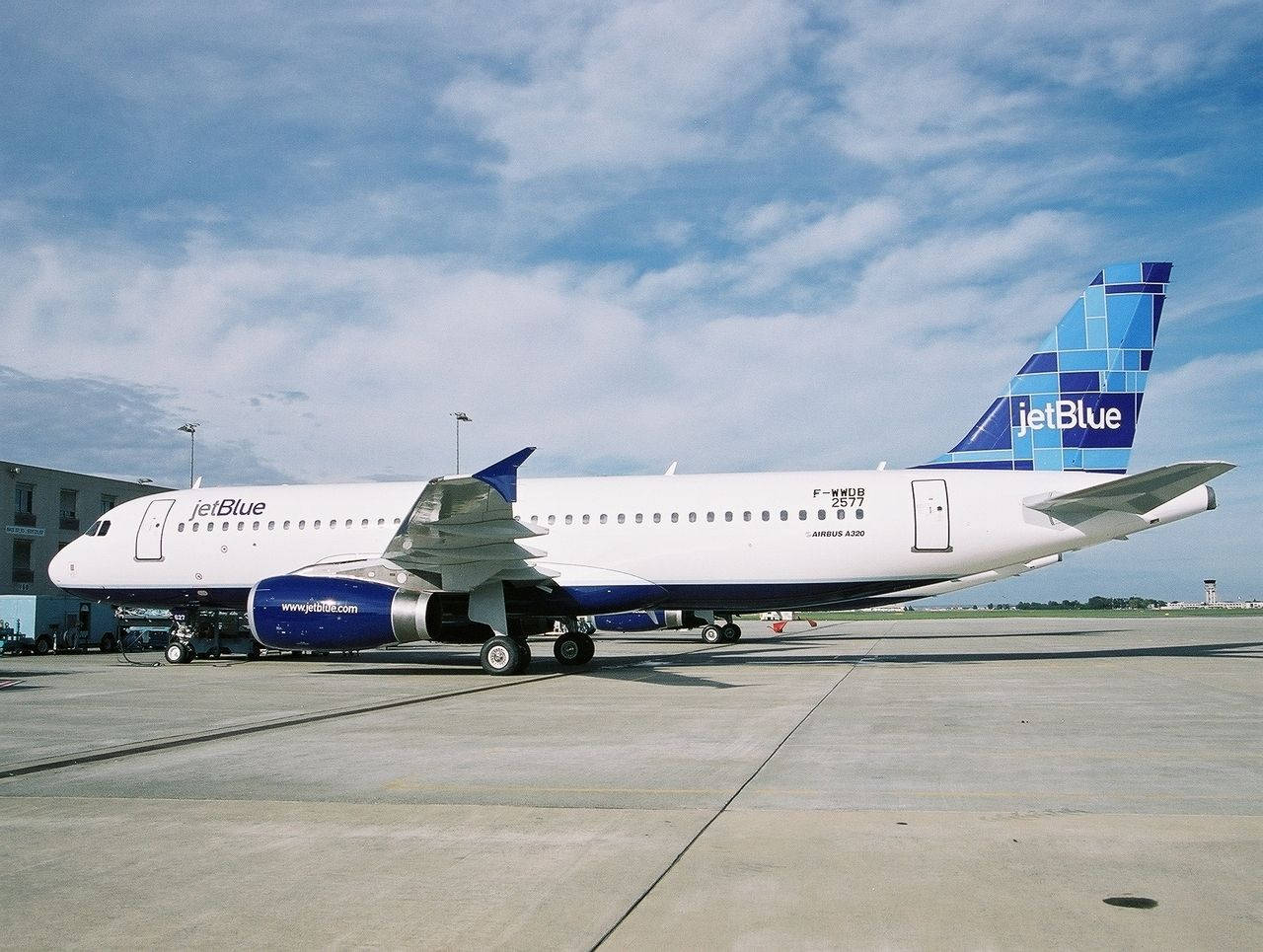 Plane 桌布 壁紙 — 一架白色和藍色的 JetBlue Airbus A320 停泊在陽光普照的機場停機坪上，天空局部多雲。
