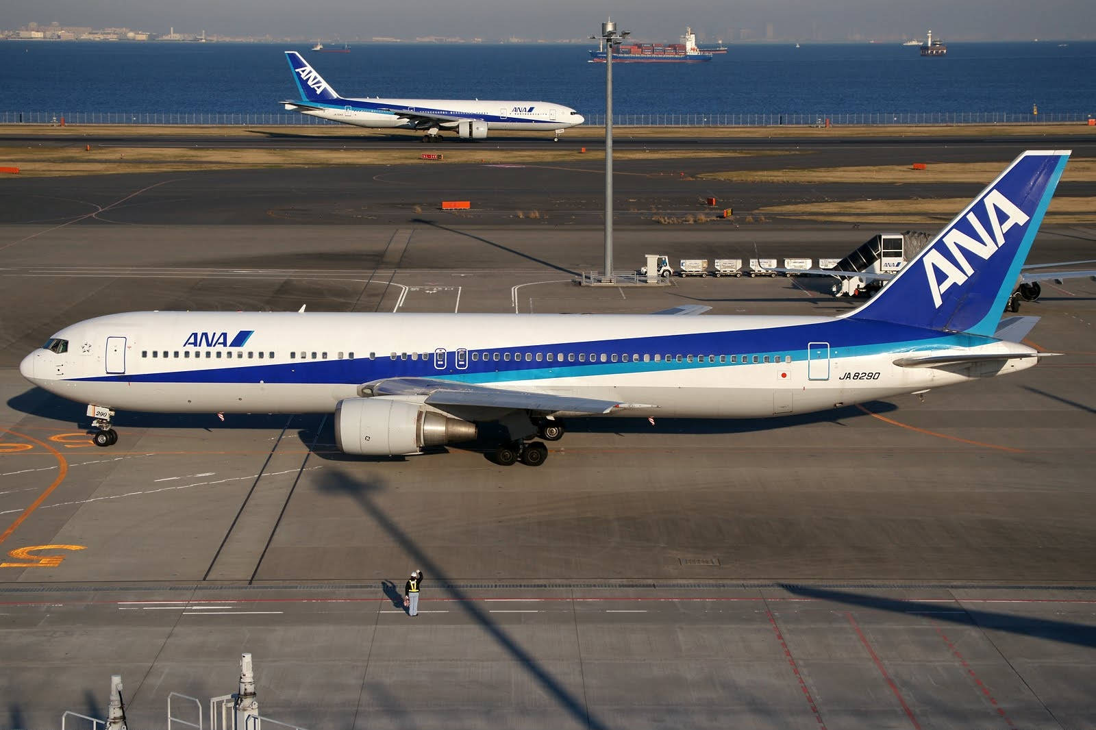 Airport 桌布 壁紙 — 一架白色和藍色的ANA飛機停在機場停機坪上，背景有另一架噴射機和海洋。