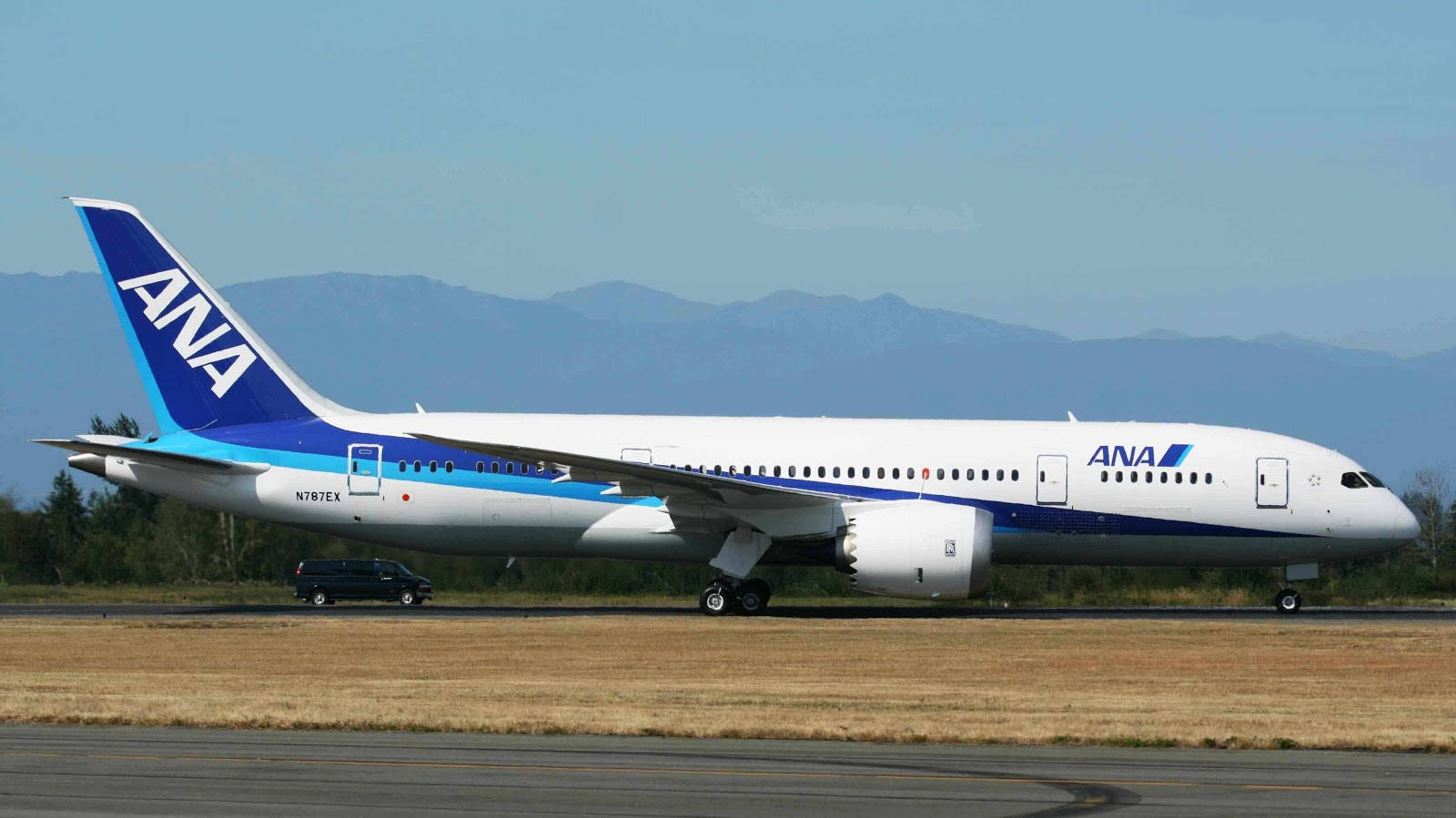 Airport 桌布 壁紙 — 一架白色和藍色的全日空波音787夢幻客機在晴朗藍天下，於跑道上滑行，遠方有山巒。